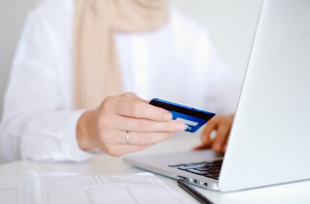 tenant in a white shirt holding a credit card in front of a laptop to make an online payment